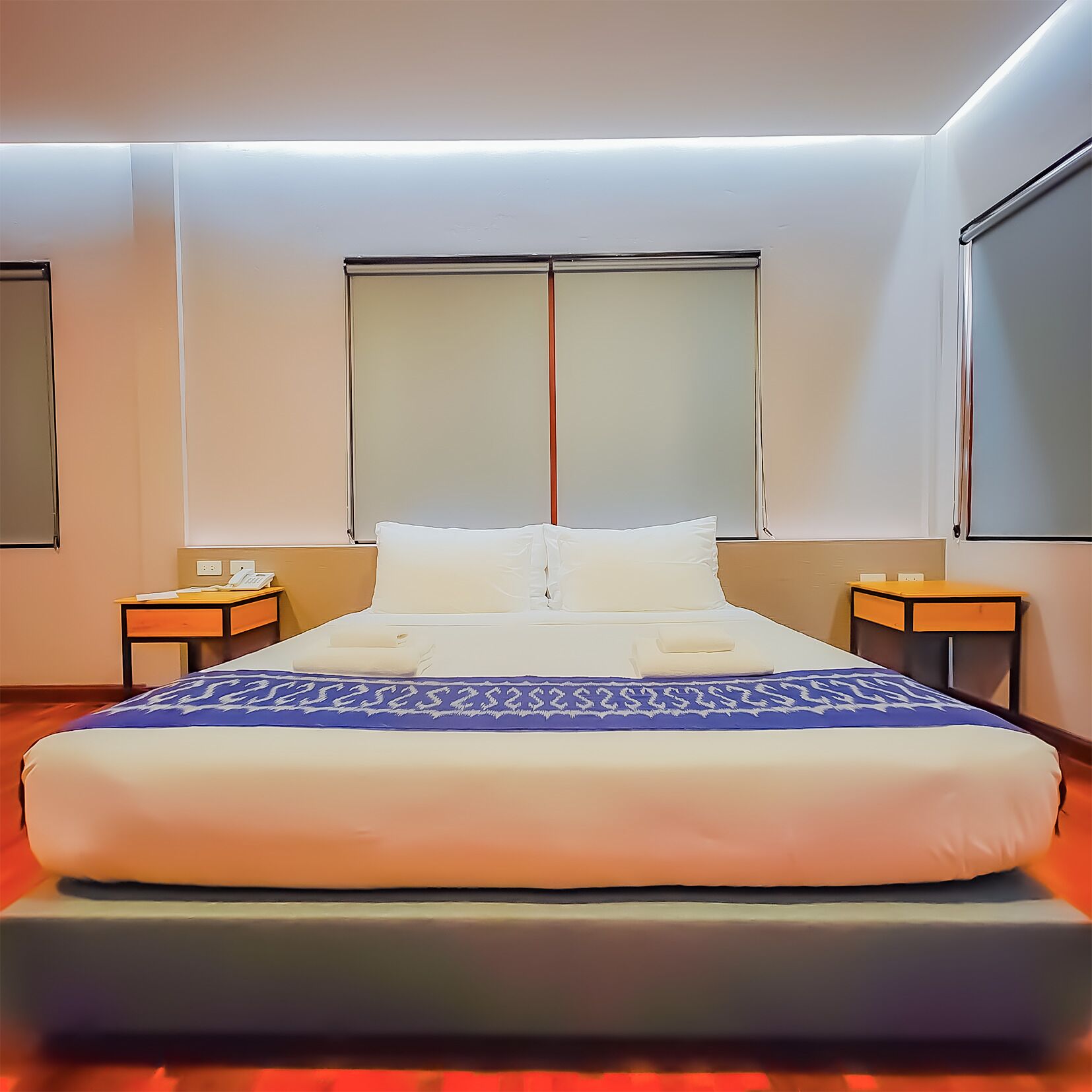 Ein modernes Hotelzimmer mit einem großen Bett, zwei Nachttischen, einem Fenster und einem an der Wand befestigten Fernseher.