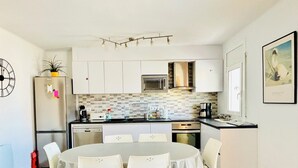 A compact kitchen with white cabinets, a microwave, a stove, and a dining area with a round table and chairs. - 2ND LINE OF THE BEACH AND THE PROMENADE OF ROSES (Roses)