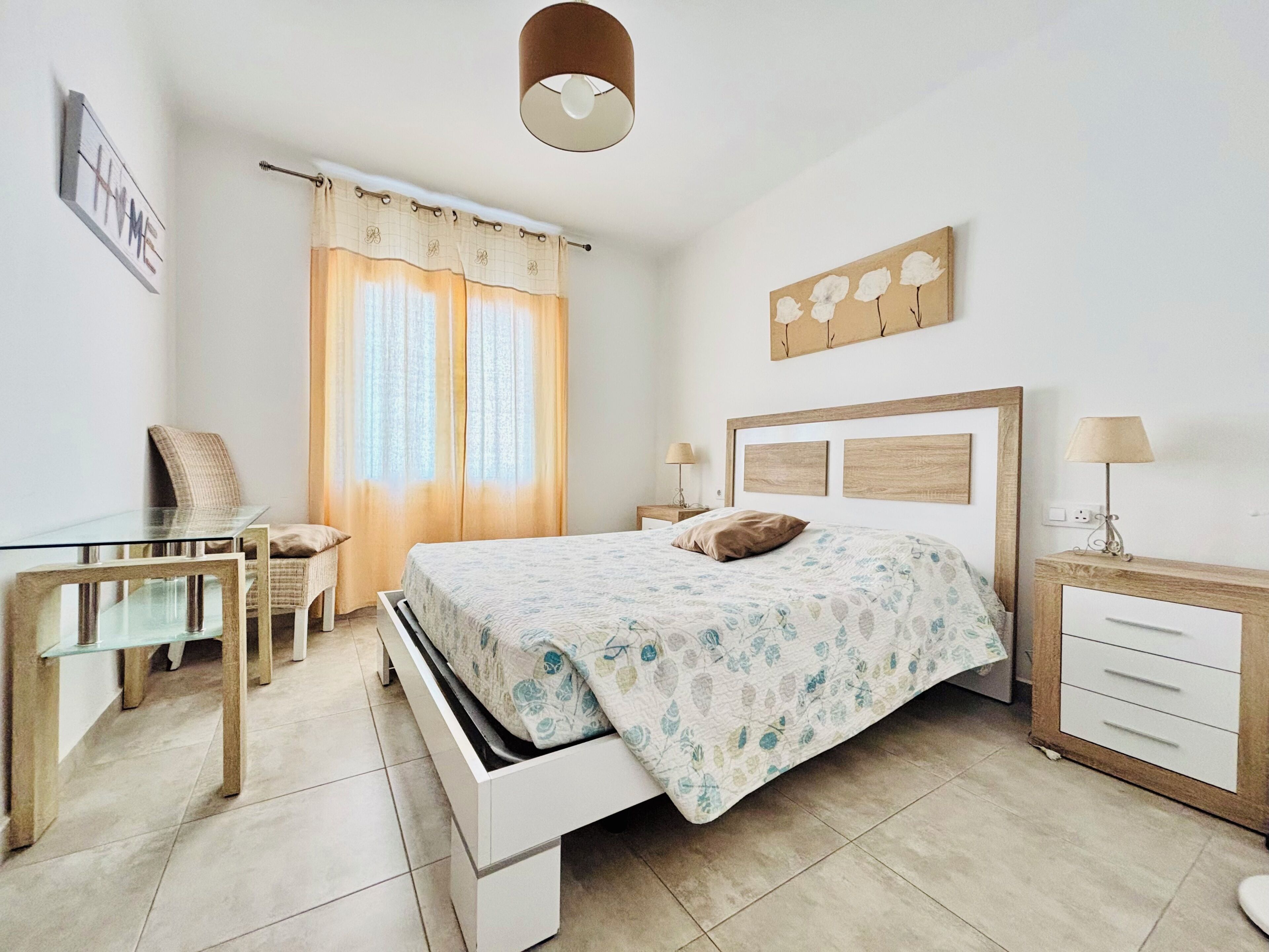 A bedroom with a bed, bedside tables, a desk, and a chair.