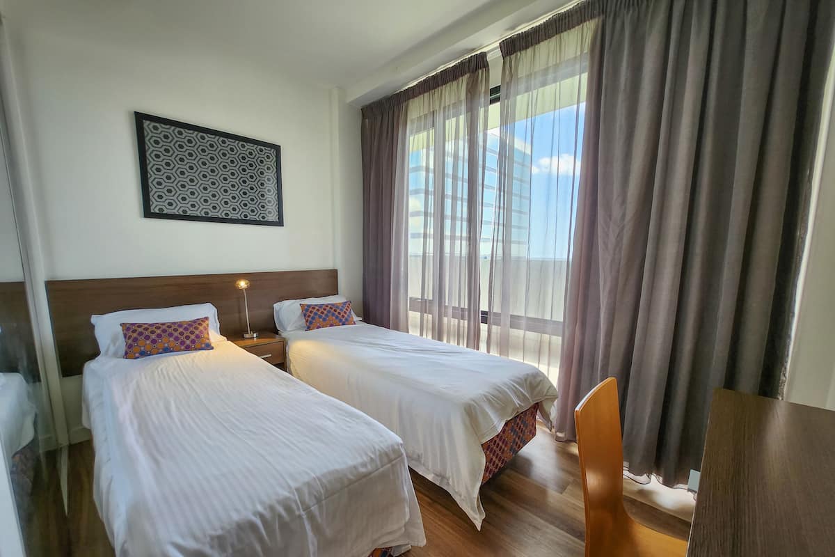 A hotel room with two beds, a nightstand with a lamp, a chair, and a window with curtains.