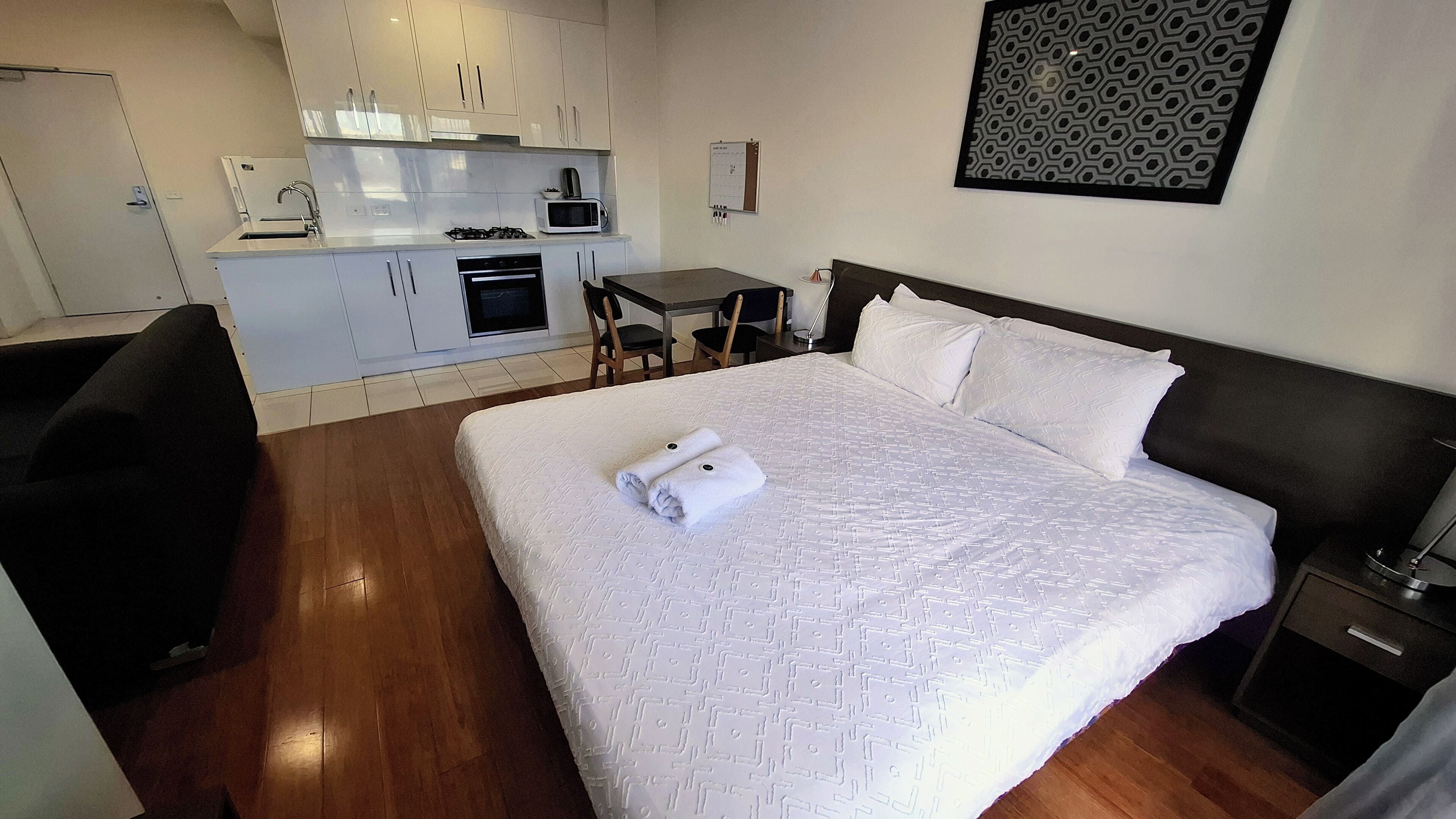 A hotel room with a bed, a small desk, a chair, a microwave, and a kitchenette.