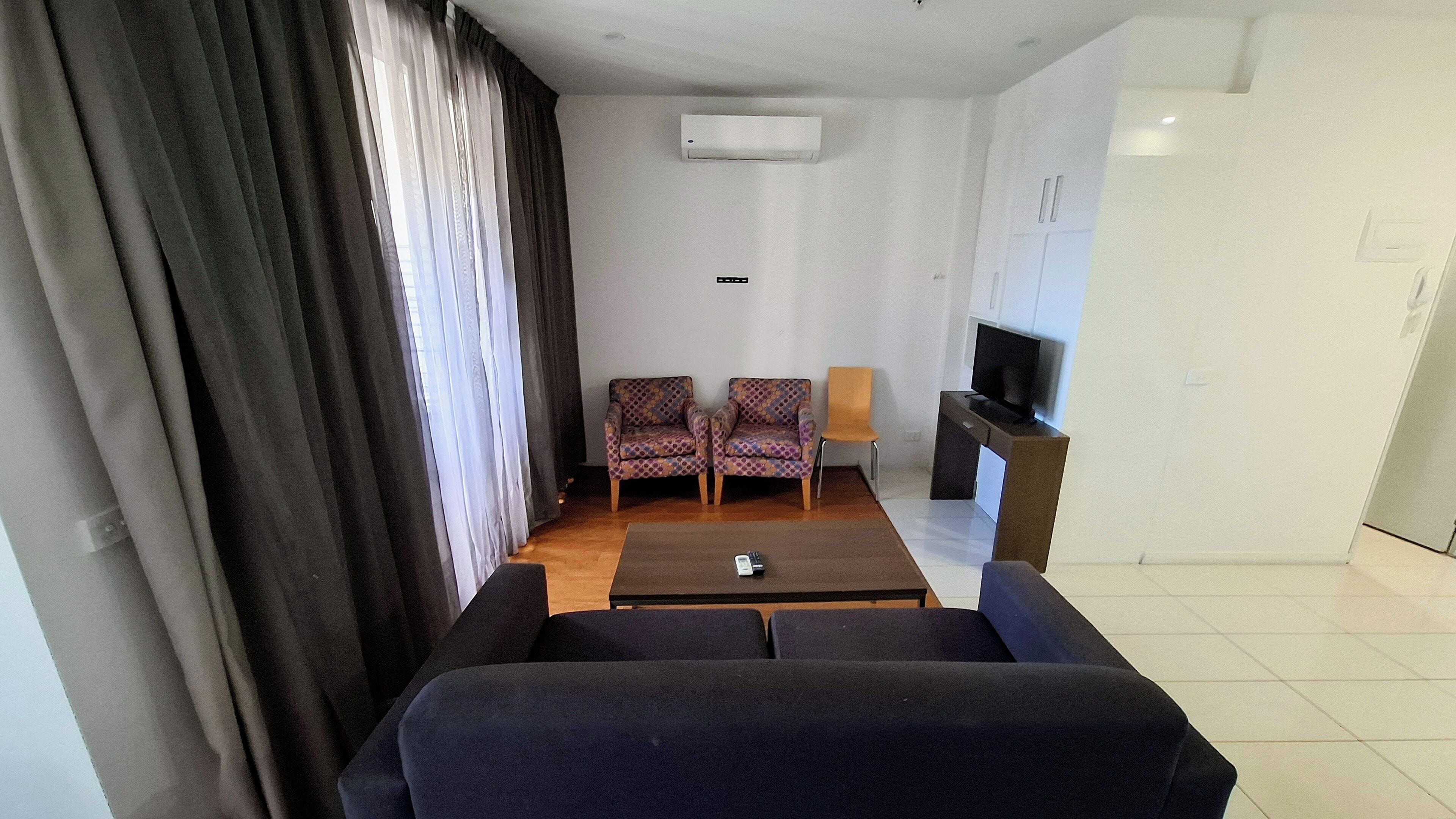 Uma sala de estar com sofá, duas poltronas estampadas, uma mesa de centro, um rack para televisão e um aparelho de ar condicionado.