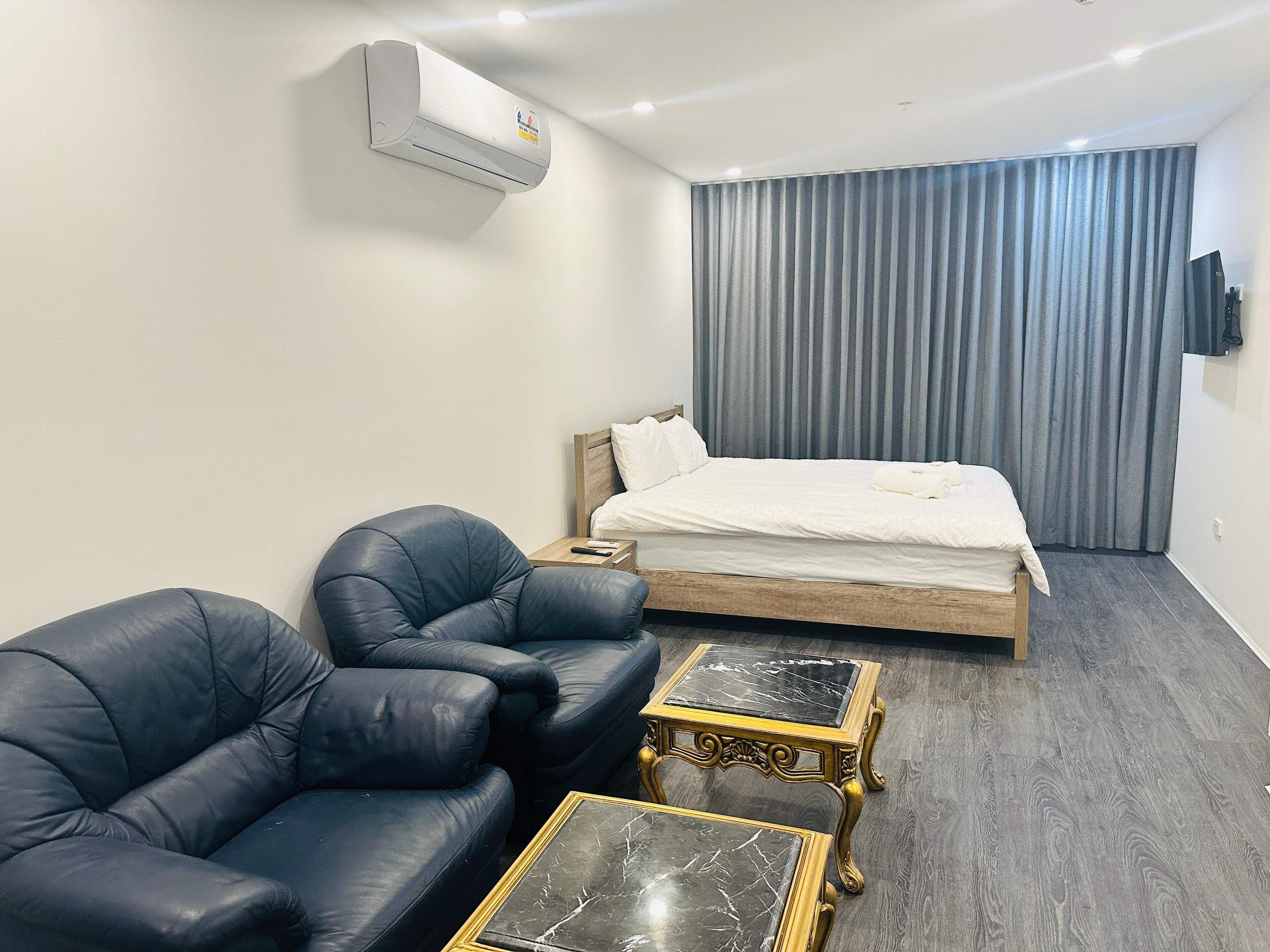 A modern hotel room with a bed, two leather sofas, a small table, and an air conditioning unit.