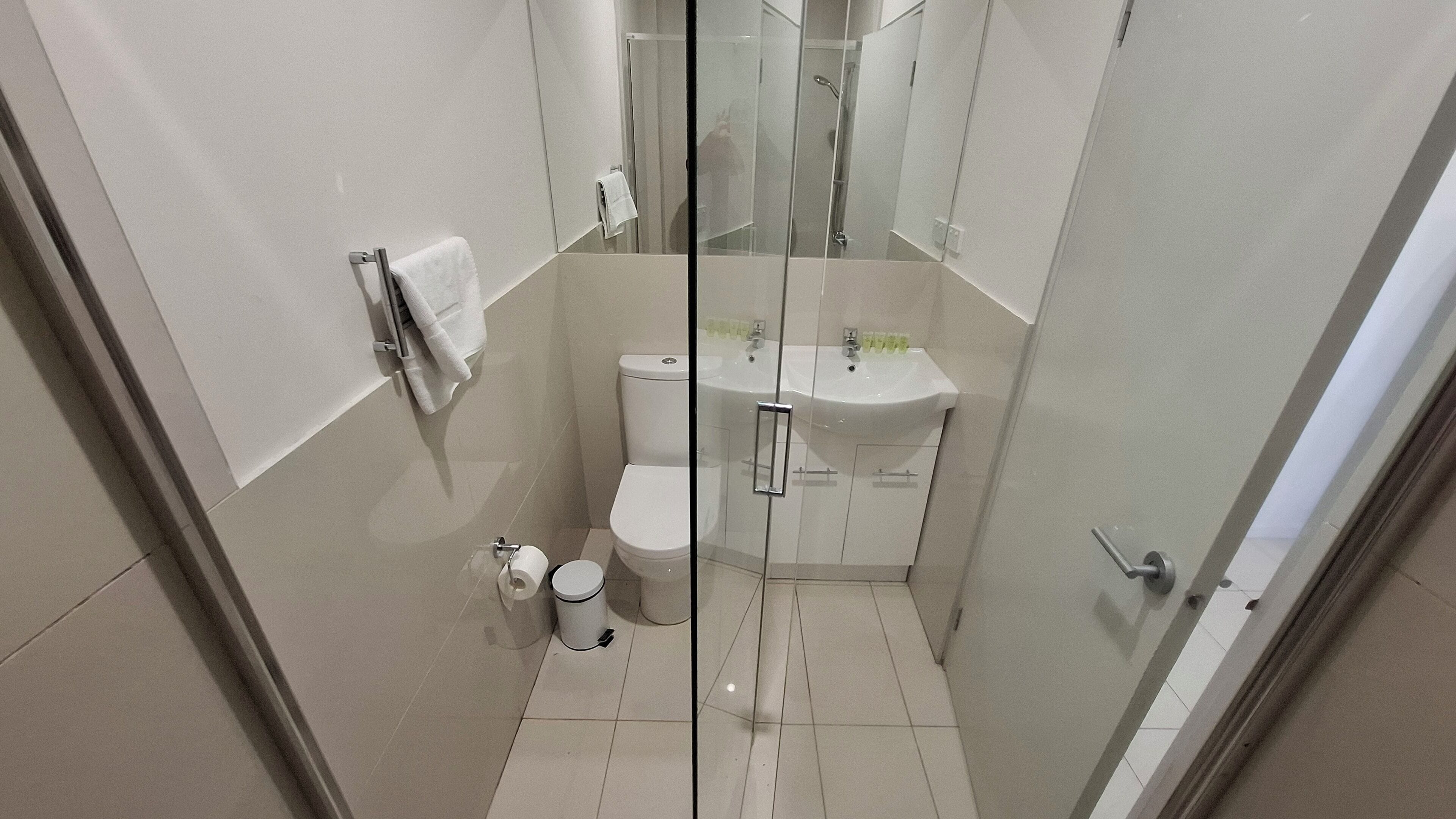A compact bathroom with a toilet, sink, and glass shower enclosure.