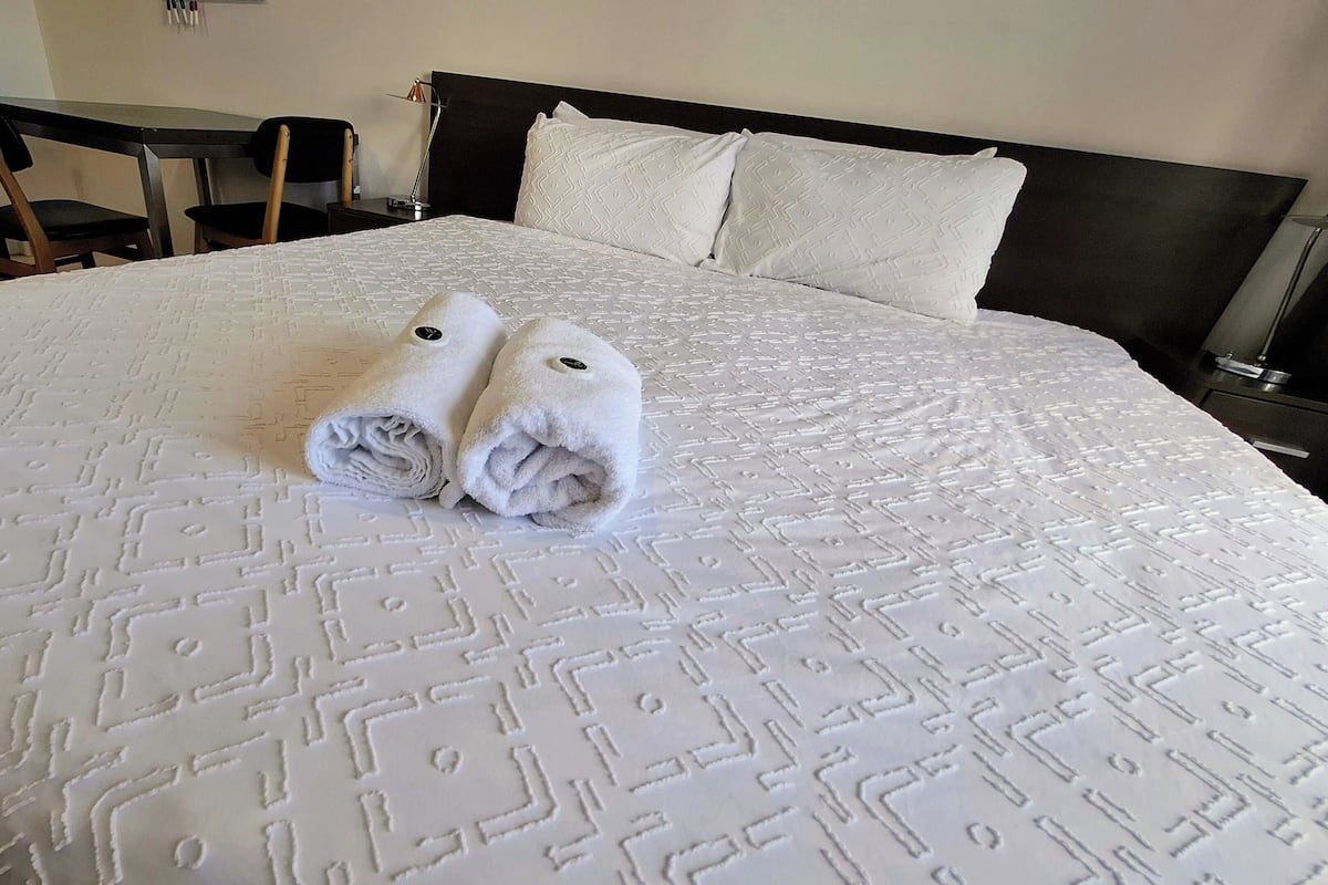 A neatly made bed with a patterned bedspread and two rolled towels placed on it.