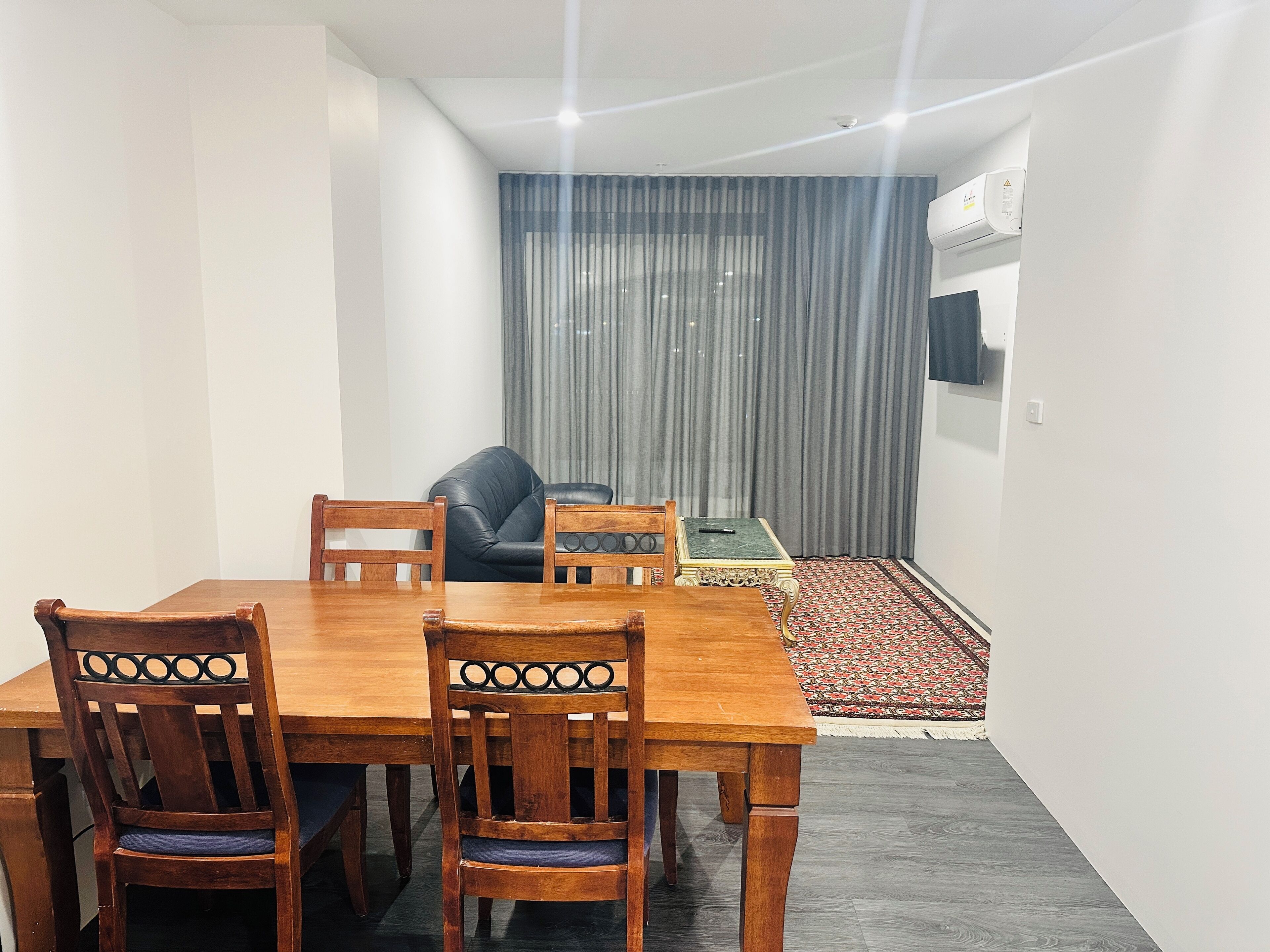 A dining area with a wooden table and chairs, a black leather sofa, and a small table with a remote control.