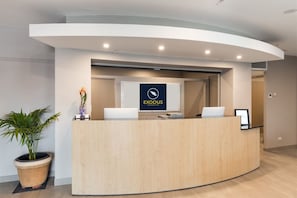 A reception desk with a logo, a potted plant, and a laptop. - Exodus Dandenong Apartment Hotel (Dandenong)