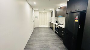 A narrow hallway leading to a kitchen with dark cabinets, a black refrigerator, and a gas stove. - Exodus Dandenong Apartment Hotel (Dandenong)