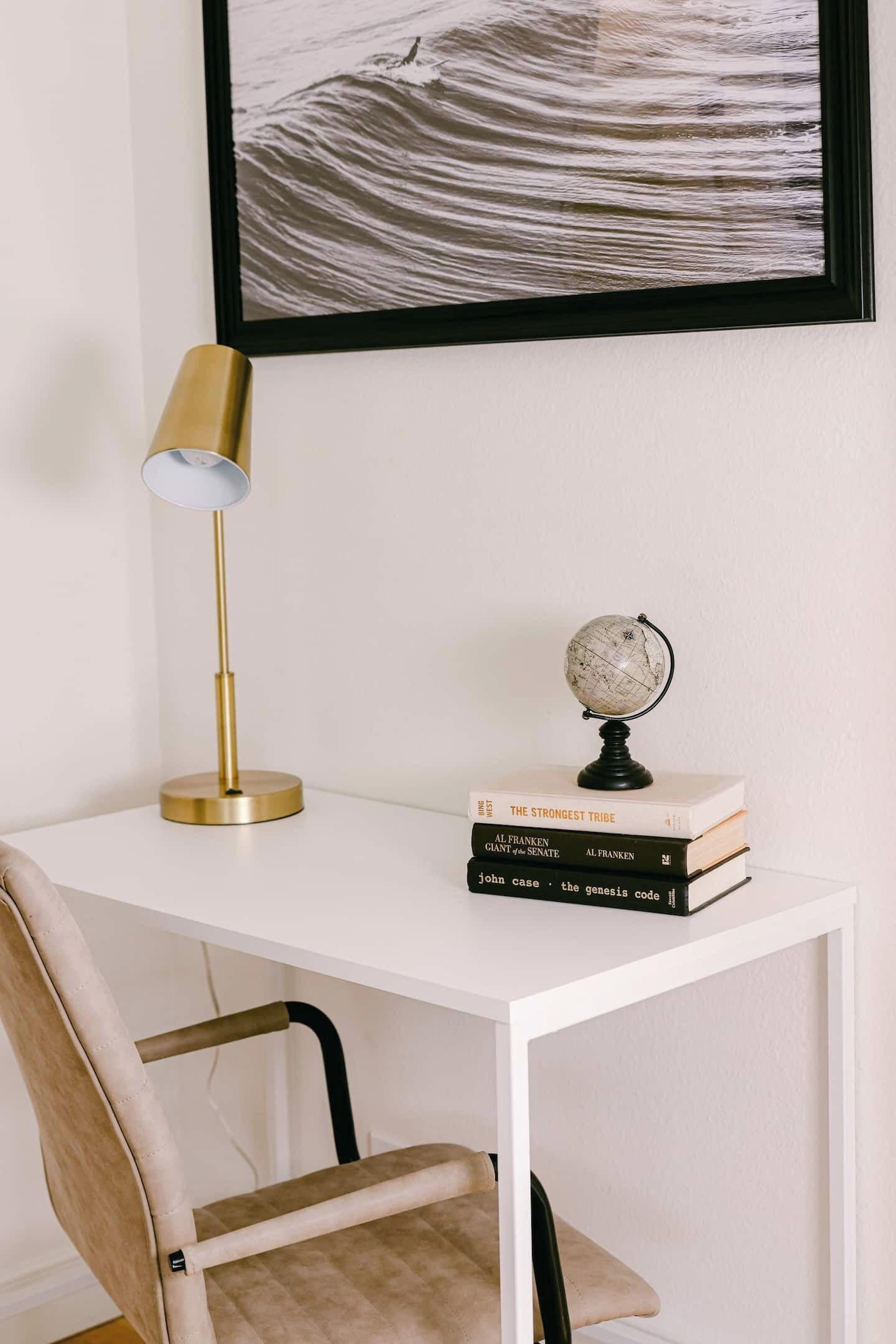 Un bureau blanc avec une lampe dorée, un globe terrestre et une pile de livres.
