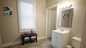 Une salle de bain avec un lavabo blanc, des toilettes, un miroir et une fenêtre avec des stores.
