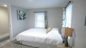 Une chambre à coucher avec un lit, une fenêtre avec des rideaux, une lampe et un tableau au mur.