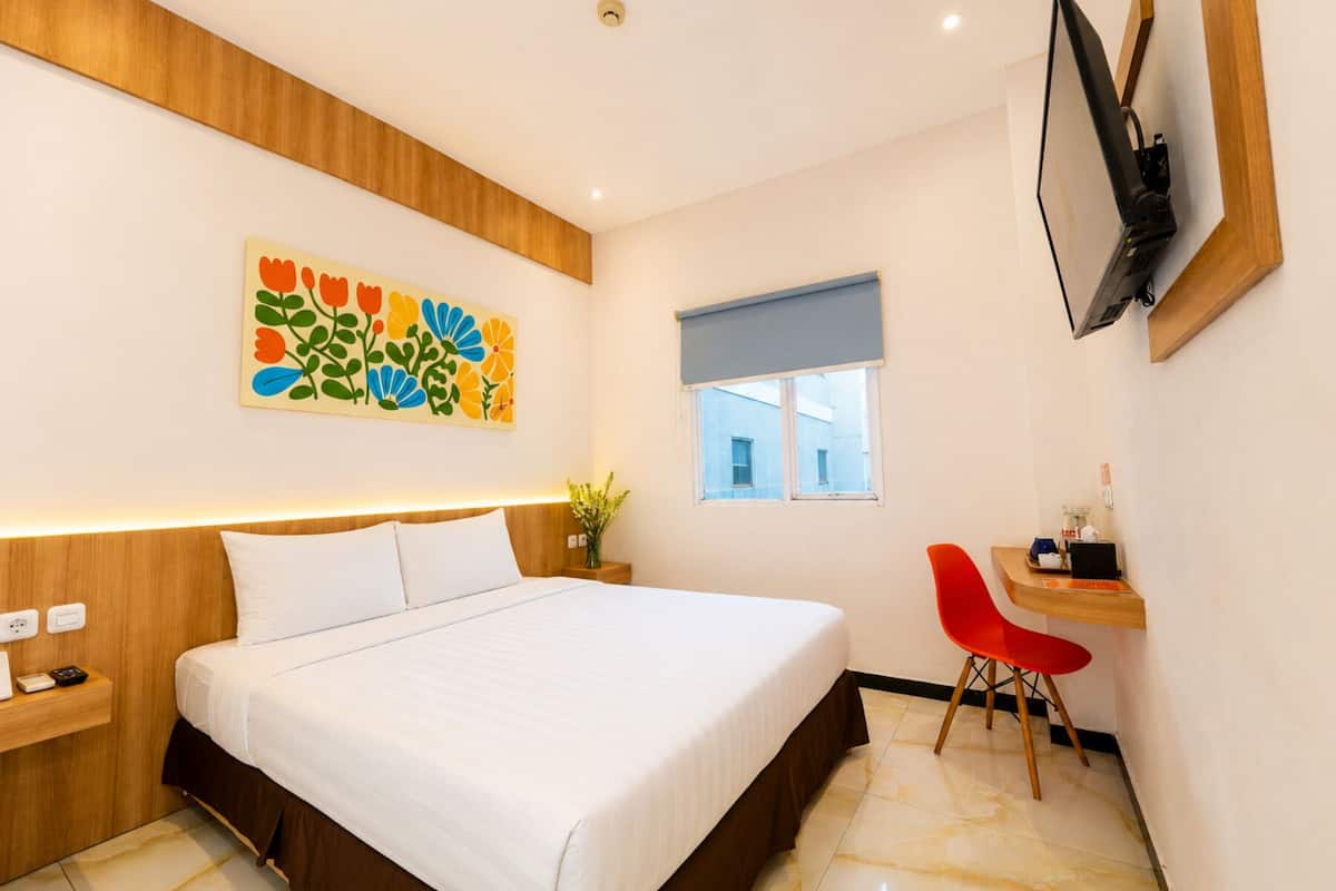 Une chambre d’hôtel moderne comprenant un lit, une table de chevet, un petit bureau avec une chaise, une fenêtre et une œuvre d’art colorée accrochée au mur.