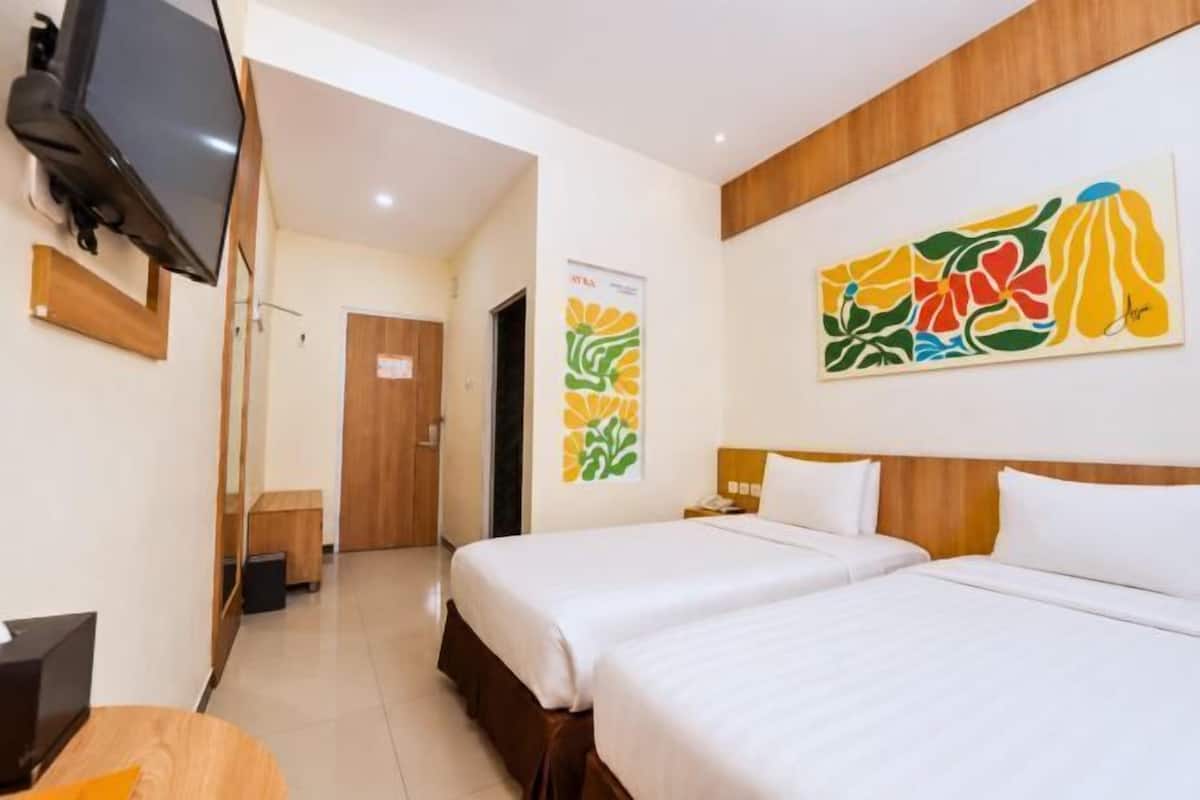 Une chambre d’hôtel avec deux lits, une télévision et des œuvres d’art accrochées au mur.