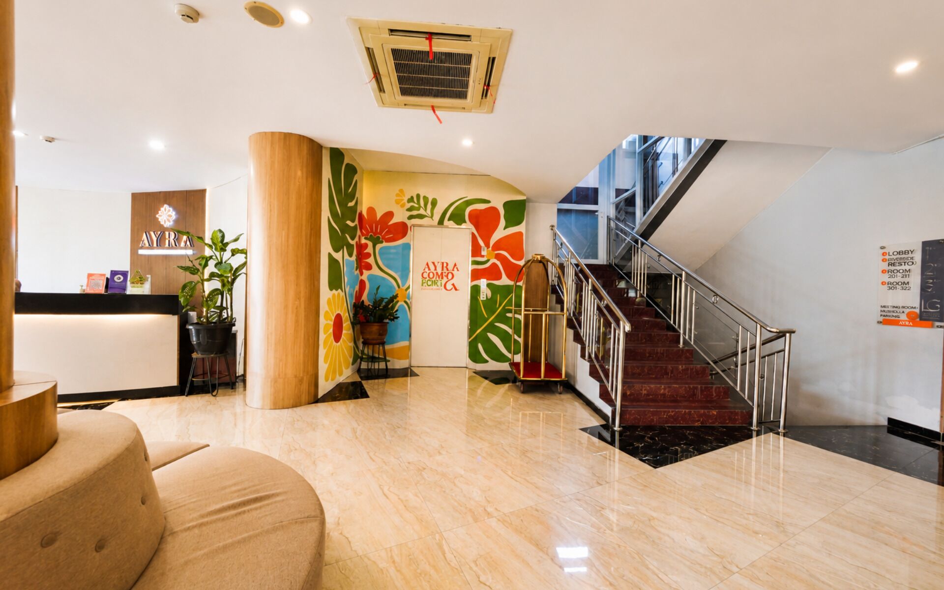 Un hall d’hôtel comprenant un comptoir d’accueil, un escalier et une fresque murale aux couleurs vives.