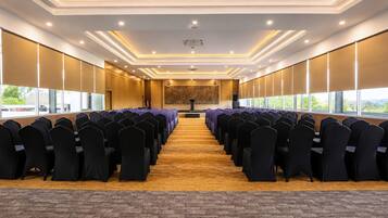 Un salón de conferencias con filas de sillas, un atril y ventanas amplias.