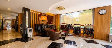 A hotel lobby with a clothing store, seating area, and a clock on the wall.