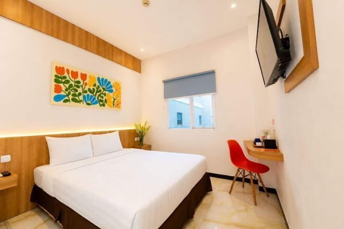 Une chambre d’hôtel avec un lit, un bureau et une chaise, un téléviseur fixé au mur et une fenêtre avec un store bleu.