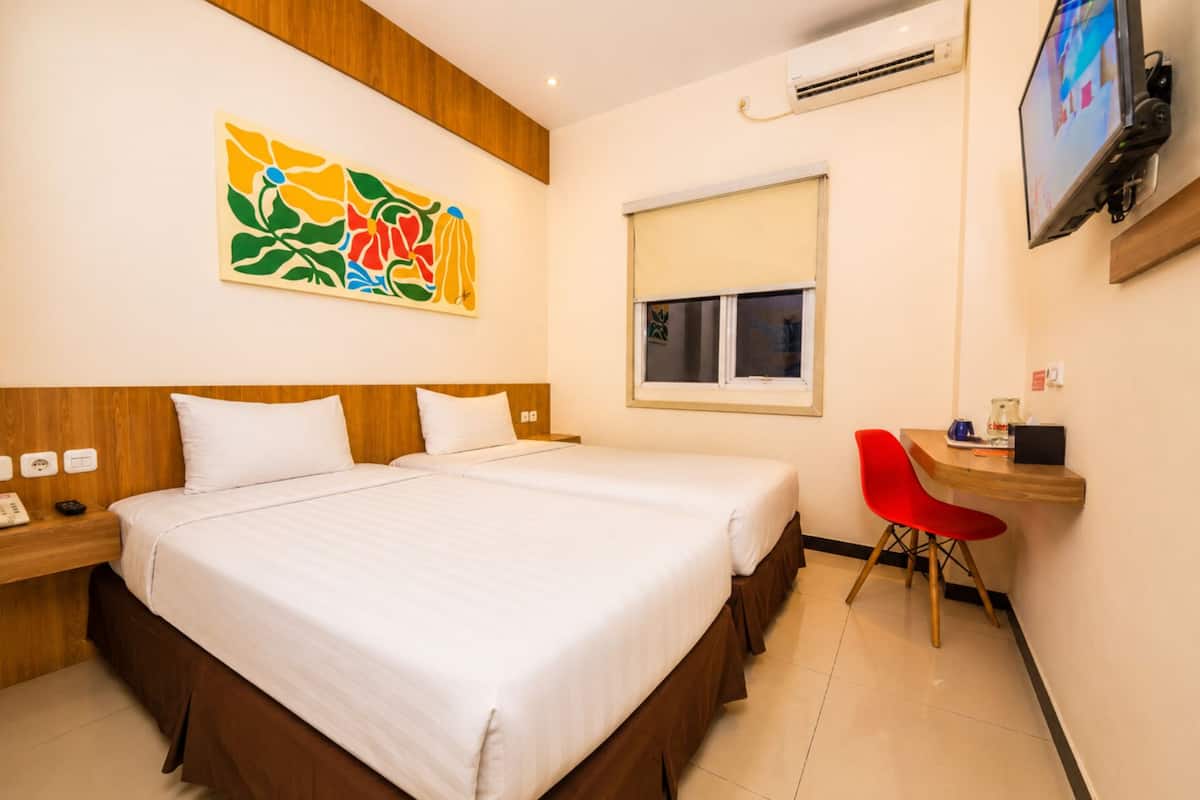 Une chambre d’hôtel comprenant un lit, un bureau avec une chaise, une télévision, un climatiseur et une fenêtre.