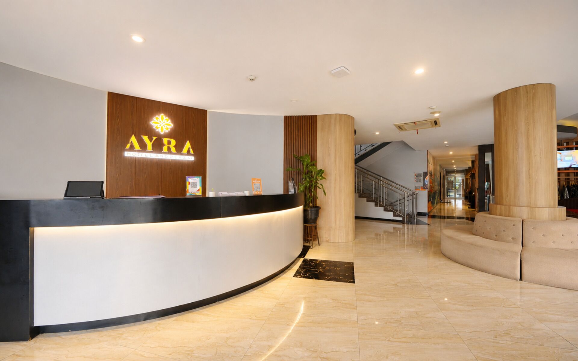 A hotel reception area with a curved reception desk, a staircase, and a large potted plant.