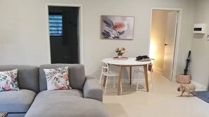 A modern living room with a grey sectional sofa, a small round table, and a ceiling fan. - Adorable 2 bedroom unit, set in lush gardens (Mcminns Lagoon)