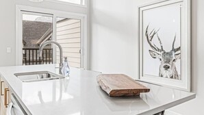 A modern kitchen with a large island, a sink, and a framed deer artwork. - Brand New 3BR with Mountain views & Private garage (Canmore)