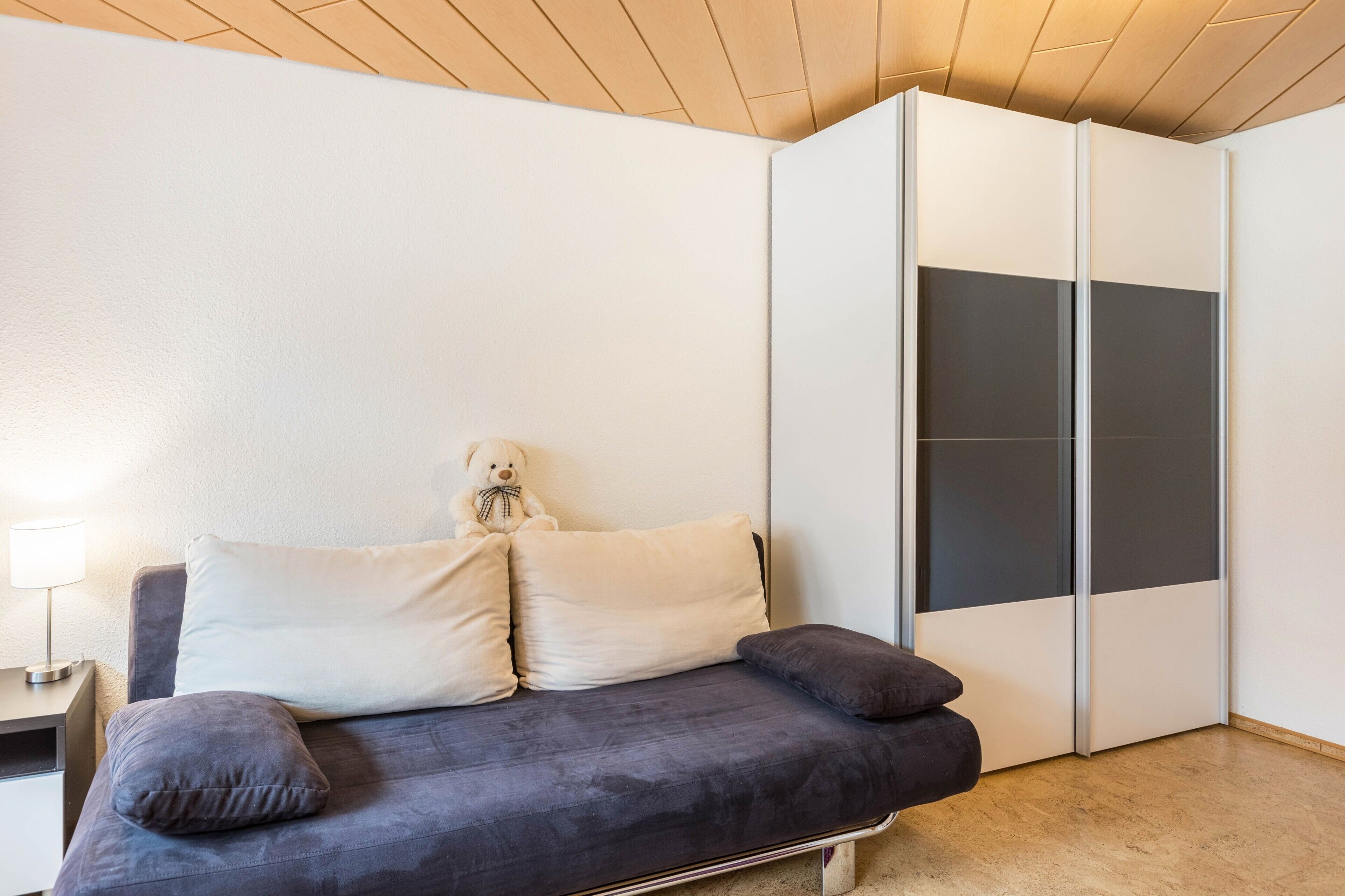 Een moderne kamer met een bank, kussens, een teddybeer en een garderobe.