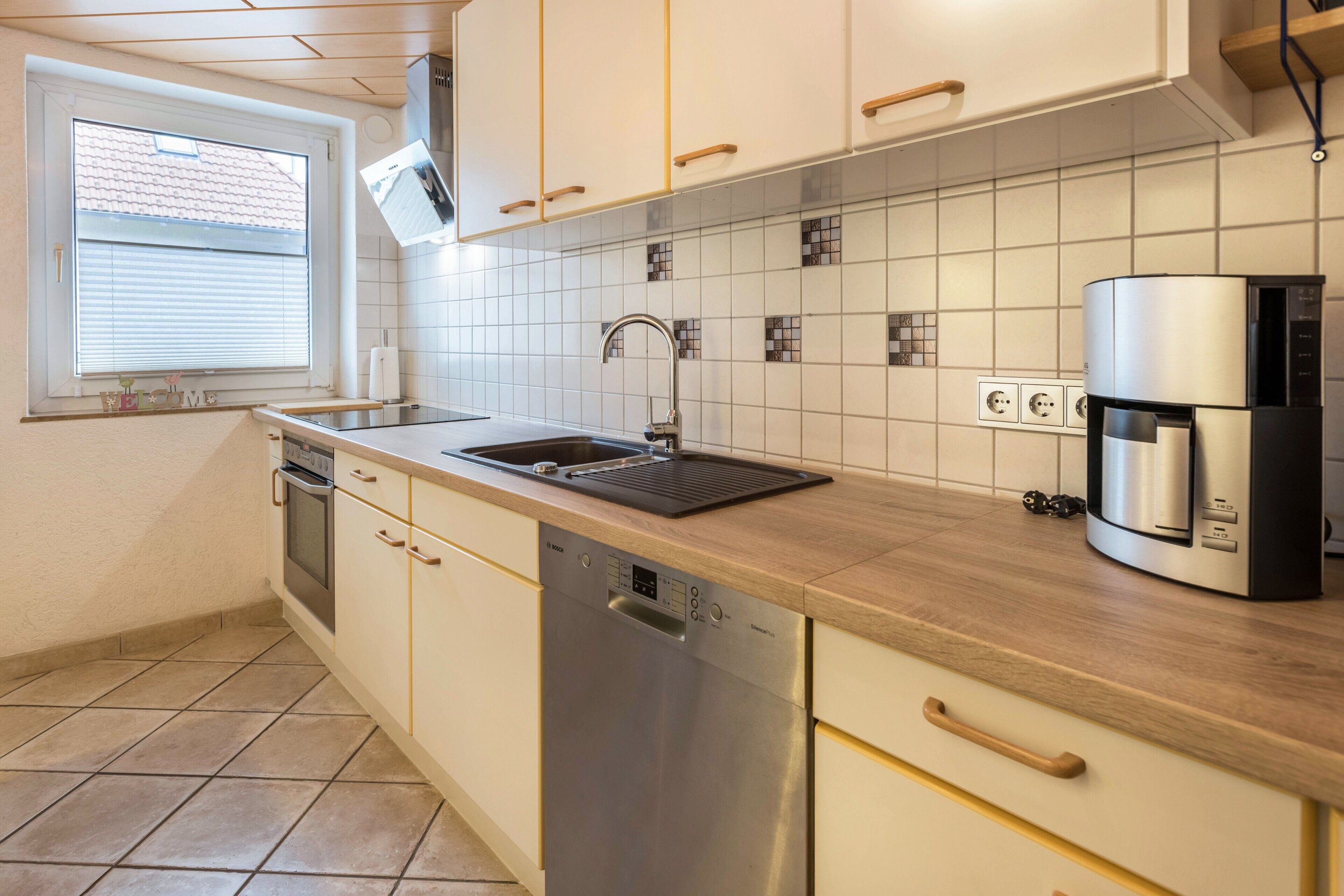 Een moderne keuken met een vaatwasser, koffiezetapparaat en betegelde spatwand.
