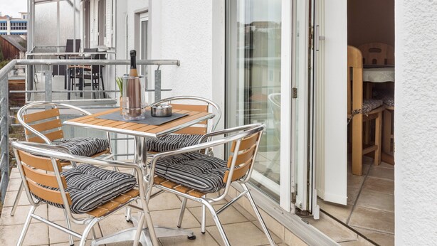 An outdoor patio with a table and chairs, a bottle, and a metal chair with a cushion. - Apartment 'Schwarzwaldblick' with Mountain View, Balcony, and Wi-Fi (St.Georgen im Schwarzwald)