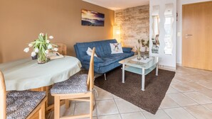 A living room with a blue sofa, a dining table with chairs, a small coffee table, a wall-mounted painting, and a wooden door. - Apartment 'Schwarzwaldblick' with Mountain View, Balcony, and Wi-Fi (St.Georgen im Schwarzwald)
