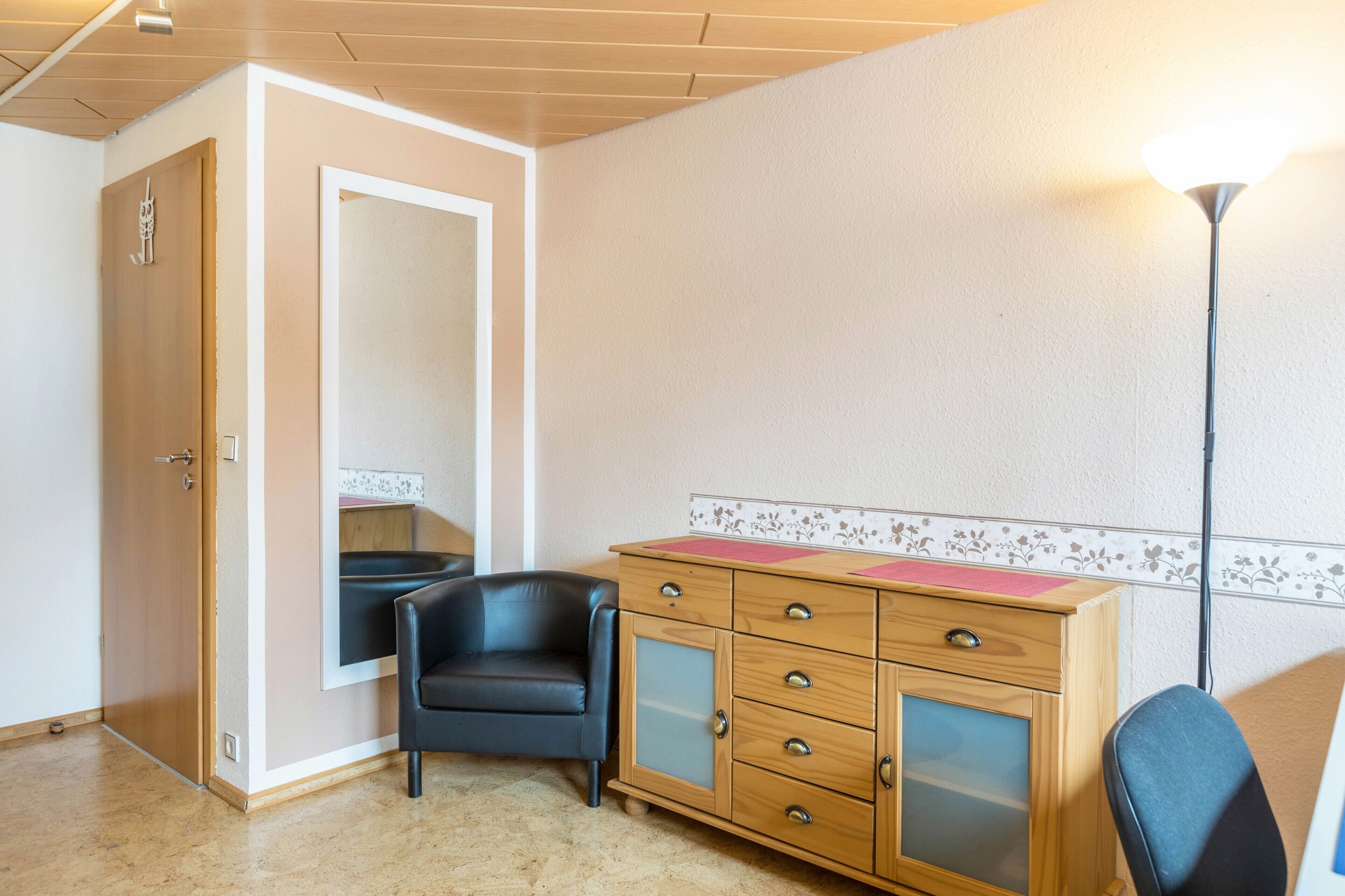 A room with a wooden cabinet, a black leather chair, a wooden door, and a wall with a floral border.
