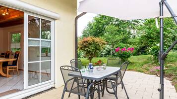 Eine Terrasse im Freien mit Tisch und Stühlen, einem weißen Sonnenschirm und Blick auf einen Garten.