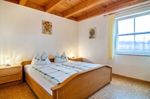 A bedroom with a wooden bed, two bedside tables, a window with curtains, and two wall-mounted paintings. - Holiday Apartment 'Beutenmühle Straussenfarm Ground Floor' with Private Terrace & Shared Garden (Owingen)