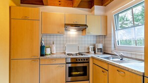 Eine Küche mit Holzausstattung, einem Herd, einem Backofen und einem Fenster mit Blick ins Grüne.