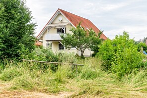 Une maison avec un toit rouge, entourée de verdure et d’une clôture en bois.