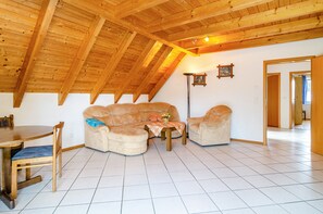 Une pièce de style loft avec un plafond haut, des poutres en bois, un ensemble de canapés, une table à manger et un lampadaire.