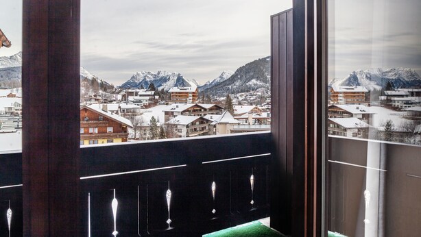 A view from a window overlooking a snow-covered mountain town with buildings and mountains in the background.