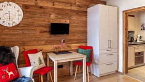 A modern kitchen with a wooden wall, a TV mounted above a small table, and a white cabinet.