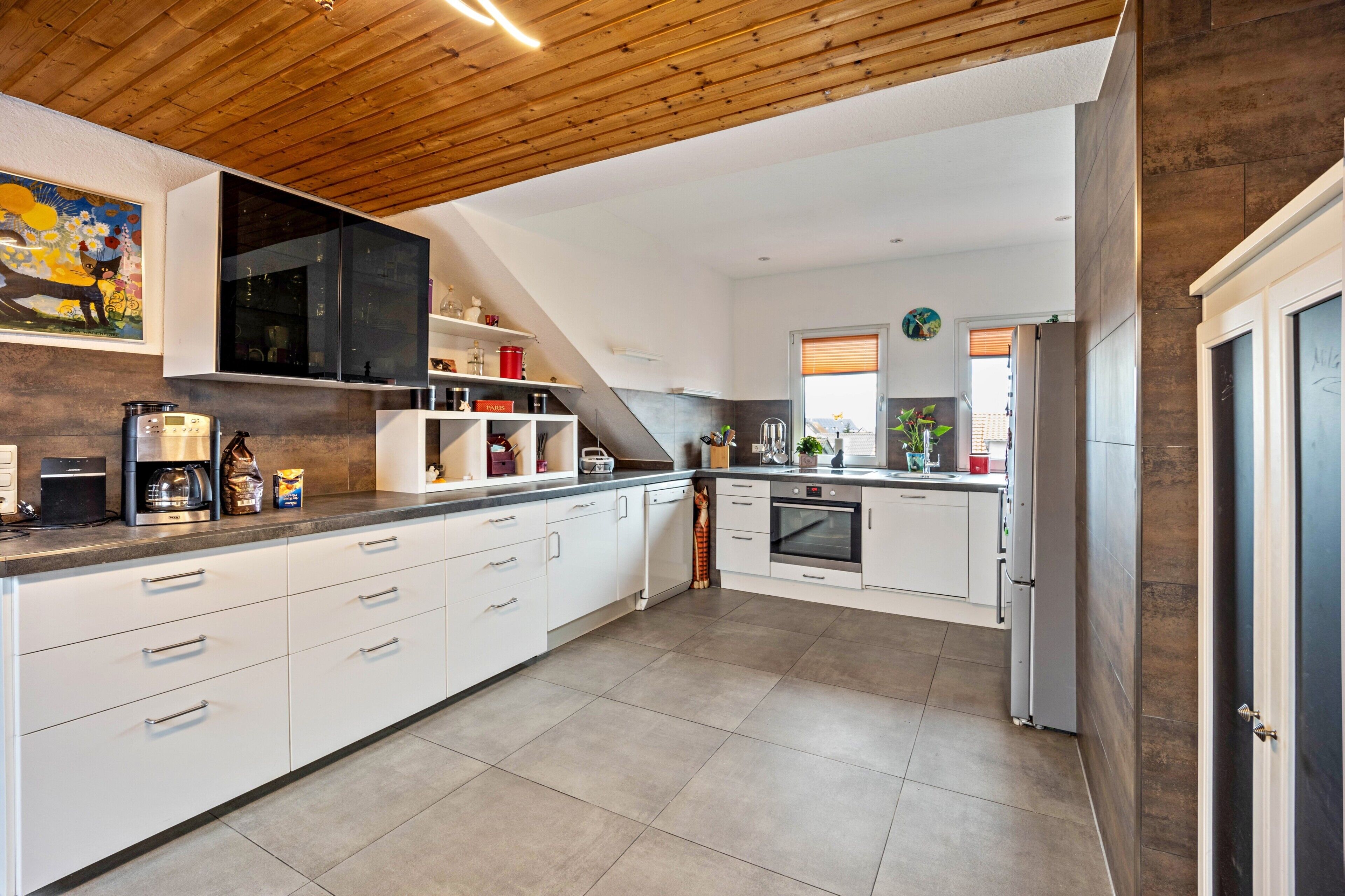 Een moderne keuken met witte kasten, een houten plafond en een inbouwoven.