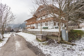 Un bâtiment recouvert de neige, doté d’un balcon en bois, d’un mur en pierre et d’un sol enneigé.