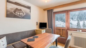 Una habitación acogedora con una mesa de madera, un sofá, un televisor y una ventana con vistas nevadas.