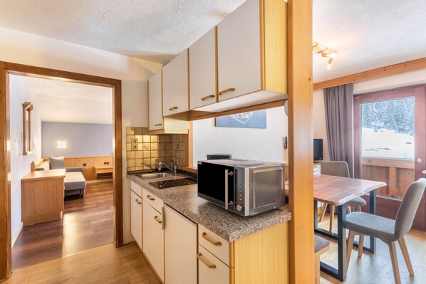 A compact kitchen with a microwave, wooden cabinets, and a dining area with a table and chairs.