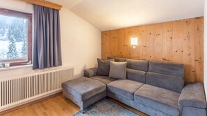 Un sofá de esquina con un panel de pared de madera, una ventana con cortinas y un radiador.