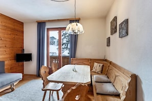 A wooden interior with a dining table, chairs, a sofa, a TV, and artwork on the wall.