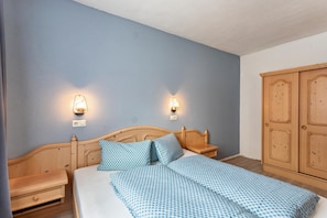A bedroom with a wooden bed, two bedside tables, a wardrobe, and wall-mounted lights.