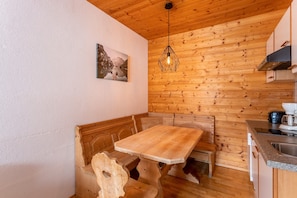 Een houten interieur met een zitgedeelte met een bank, een houten tafel, een hanglamp en een keukenwerkblad.