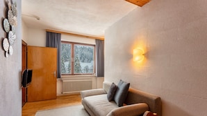A modern living room with a sofa, a wooden door, a radiator, and a window with a view of snow-covered trees. - Krafttal Kelchsau – Where Nature Gives You Strength and Every Moment Feels Like Home (Kelchsau)