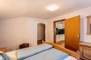 Una camera da letto con un letto, un comodino in legno, un piccolo armadietto in legno e una porta che dà su una cucina.