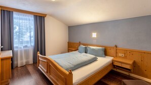 Une chambre à coucher avec un lit en bois, une table de chevet, une commode, une fenêtre avec des rideaux et un lampadaire fixé au mur.