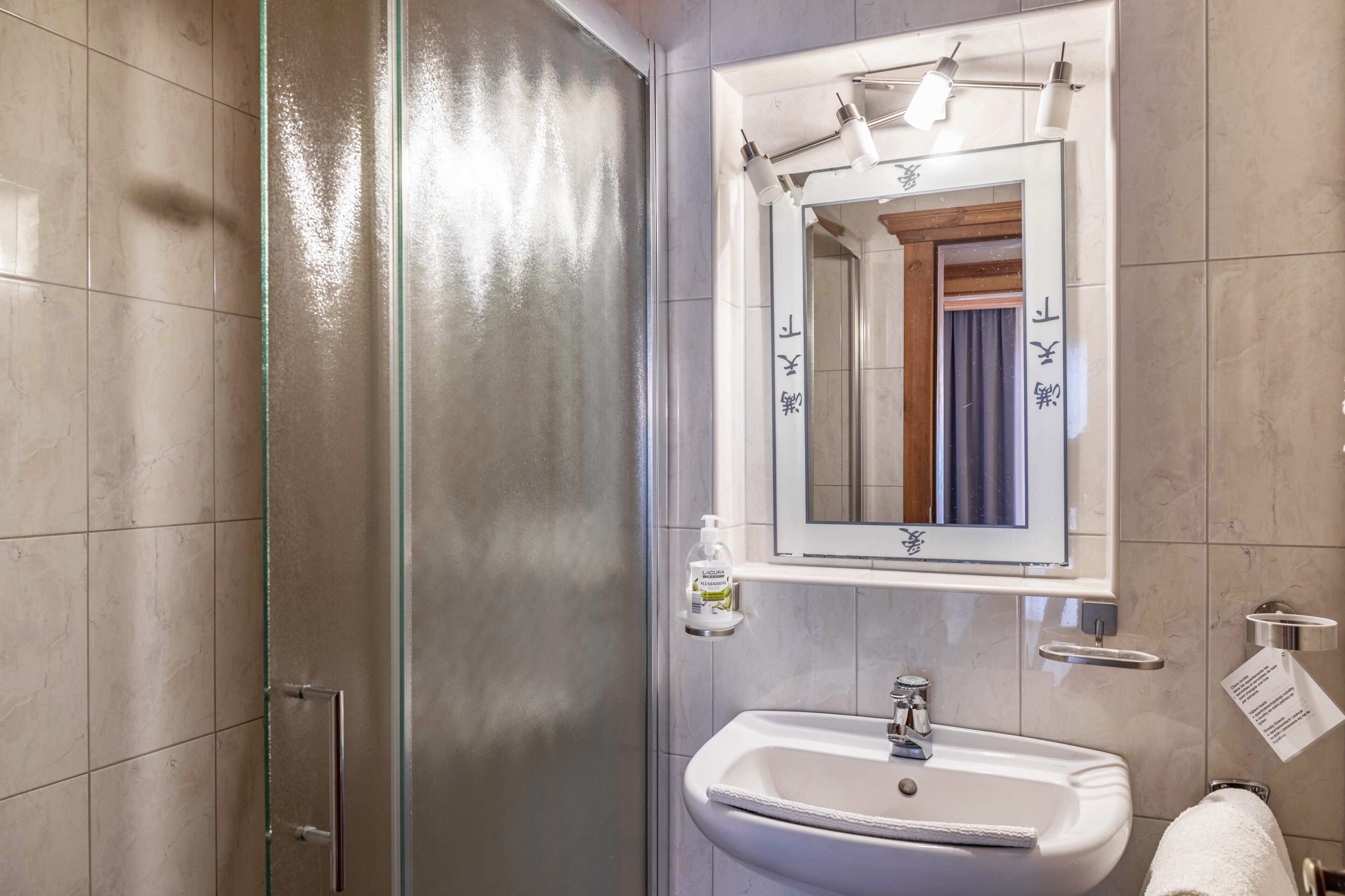 Een badkamer met een douchecabine van glas, een wastafel, een spiegel en een zeepdispenser.