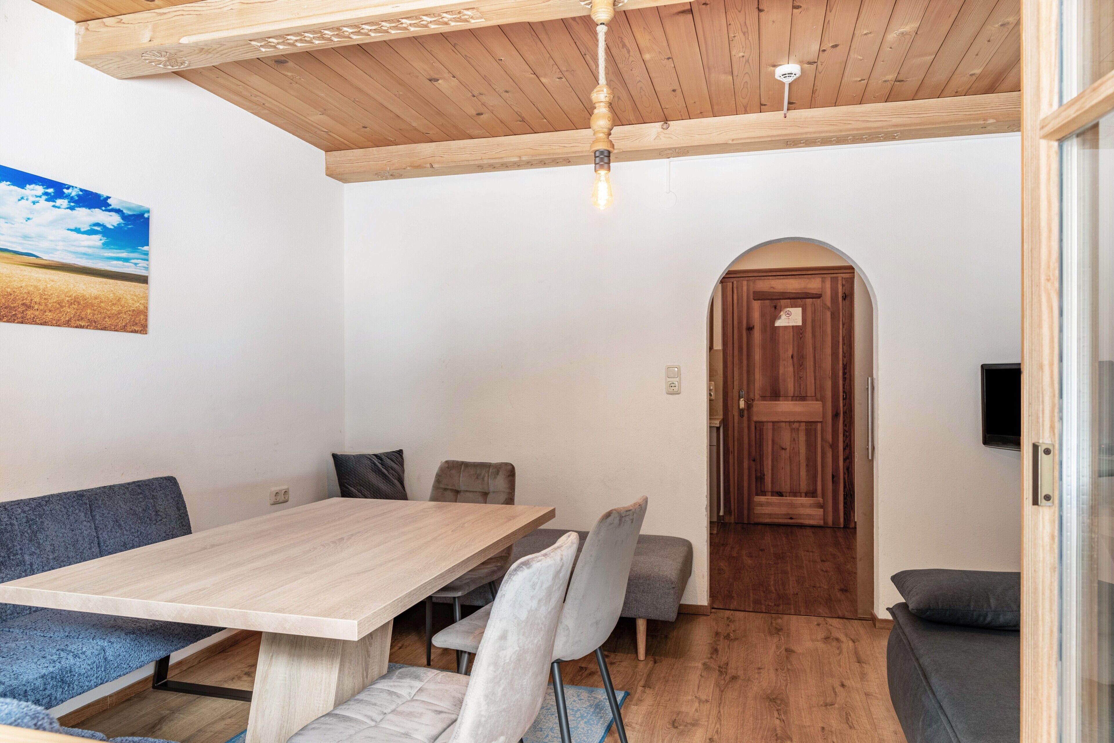 Una habitación con techo de madera, una mesa de comedor con sillas, un sofá y una puerta de madera.